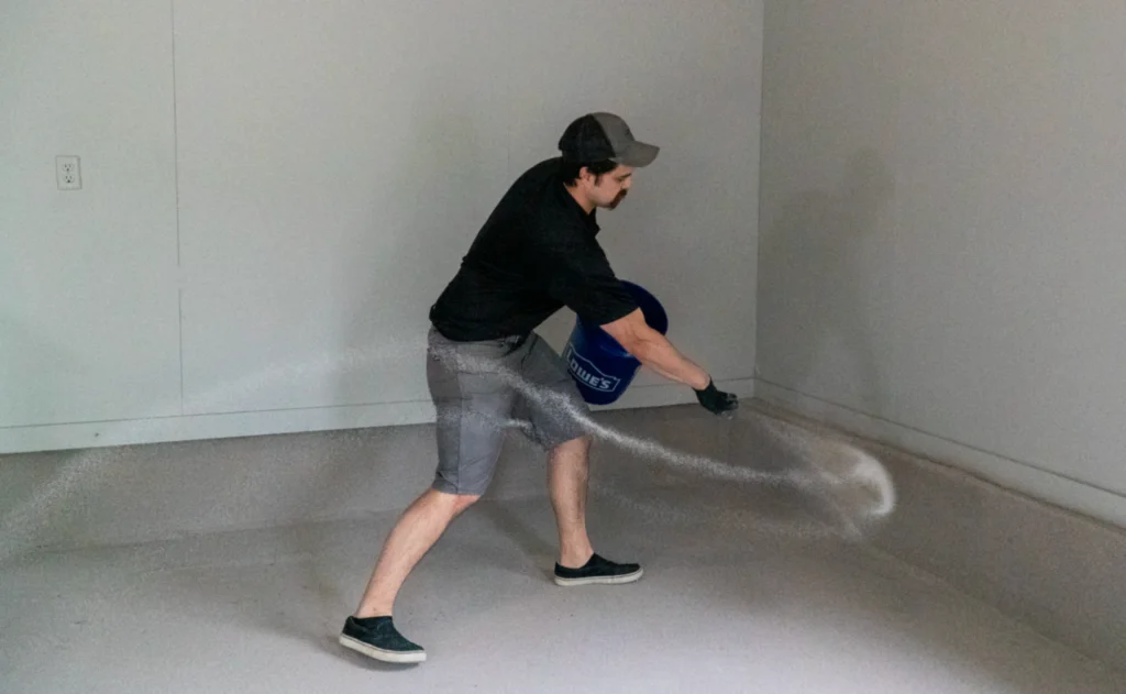Garage floor coating installer broadcasting decorative vinyl flake chips onto freshly applied polyaspartic basecoat