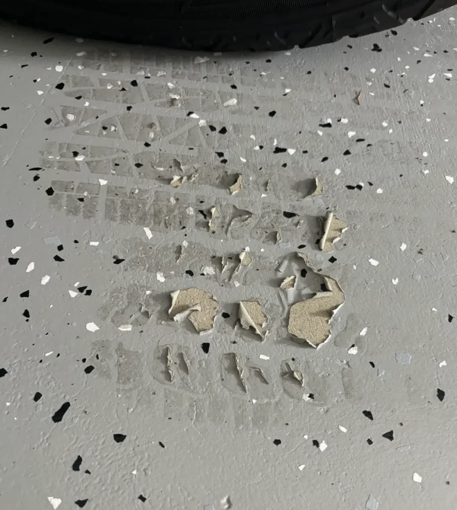 Hot tire pickup damage on DIY epoxy garage floor showing peeled coating and exposed concrete from summer tire heat transfer