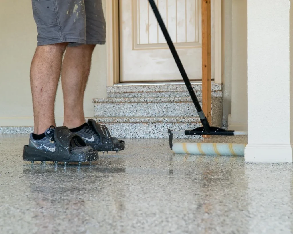 Garage Flex installer wearing spiked shoes applying polyaspartic basecoat with roller on prepped Kansas City garage floor